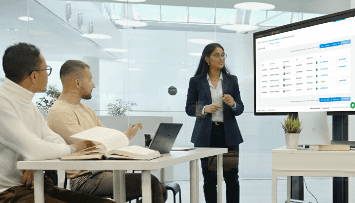 Modern office setting with diverse professionals collaborating around a digital dashboard on a large screen, showing a calendar and assignment interface