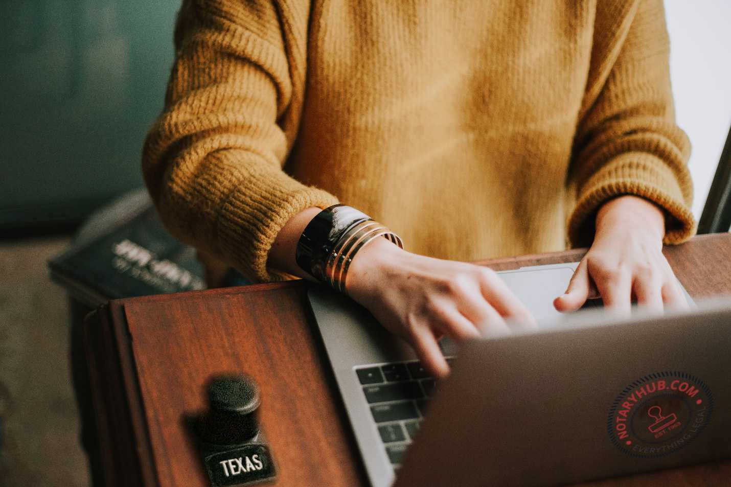 Professional woman in orange sweater working on laptop at desk, representing remote online notary services and digital transformation